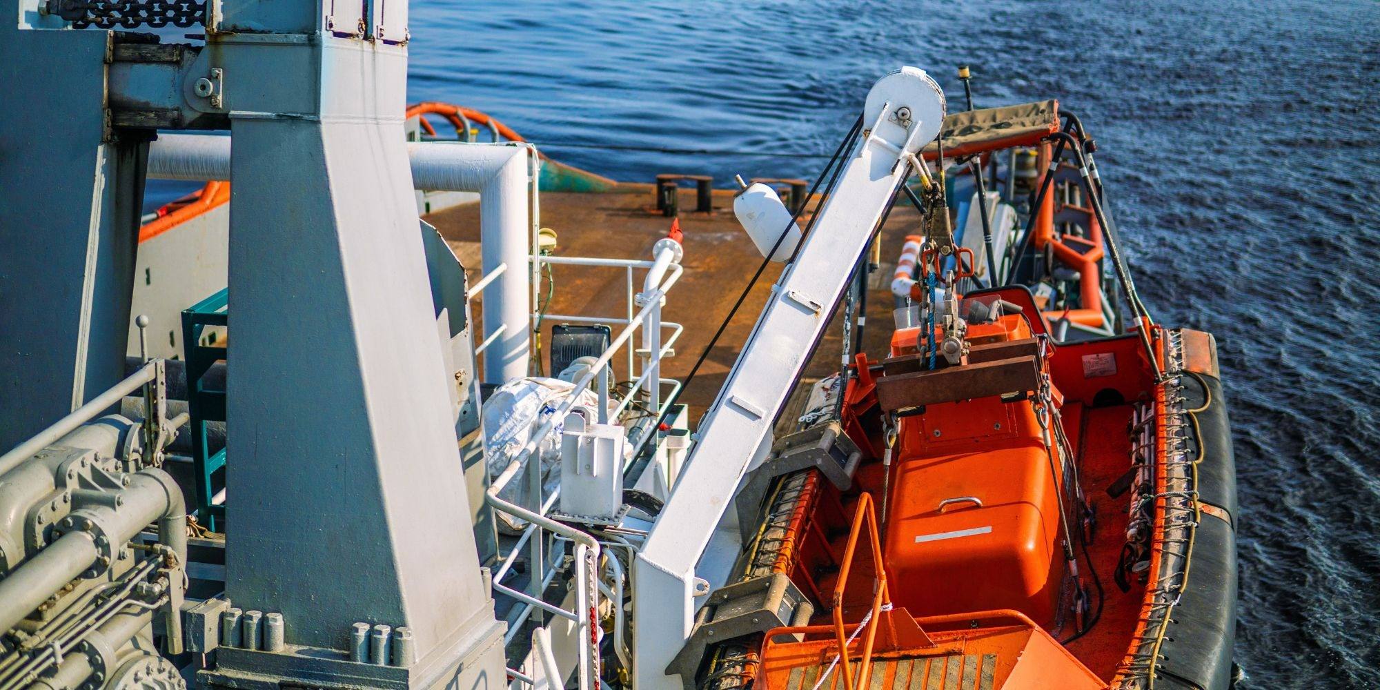 A crane and orange lifeboat mounted on the deck of a vessel