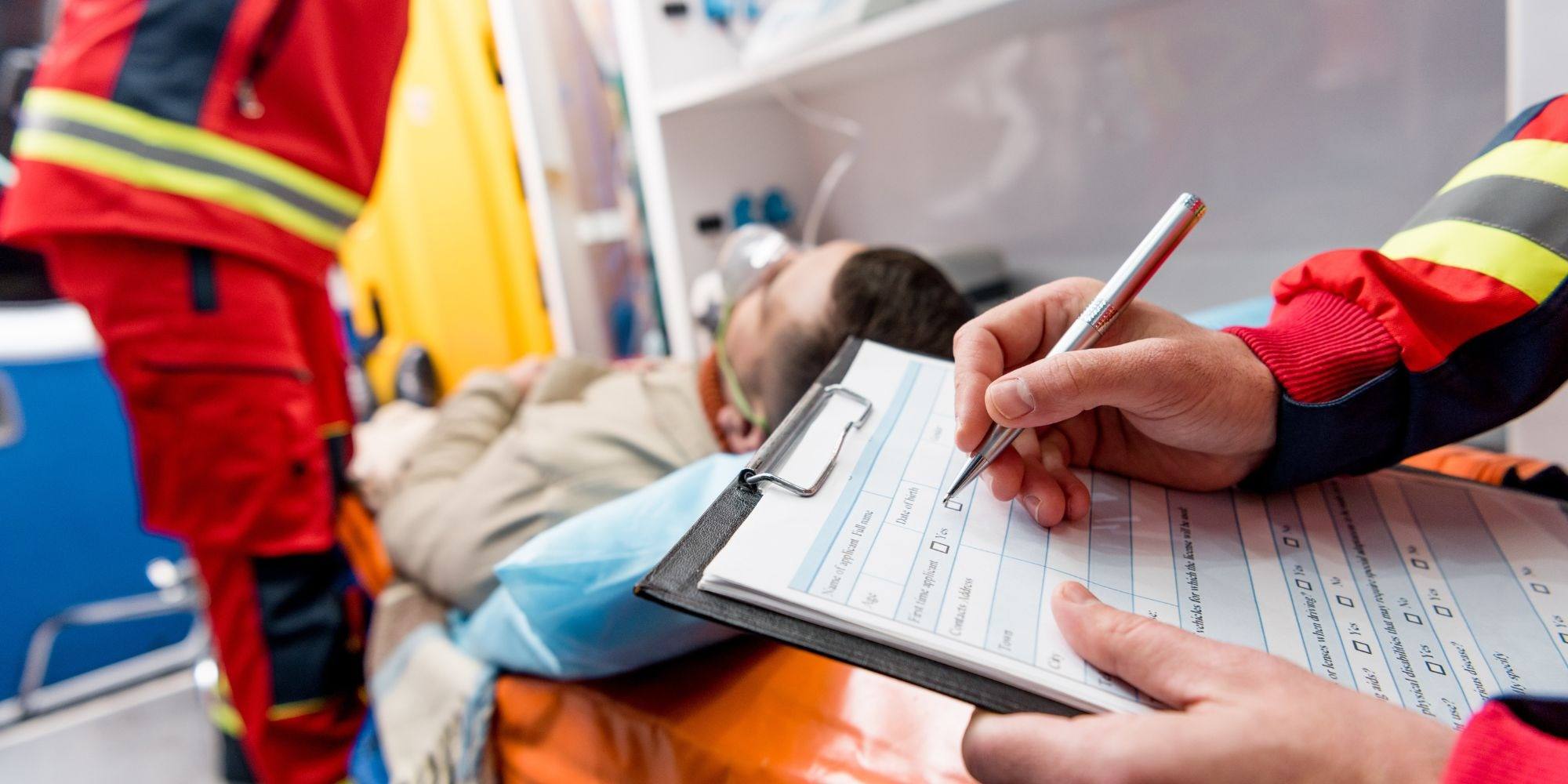 A paramedic writing on a clipboard next to a patient in the back of an ambulance